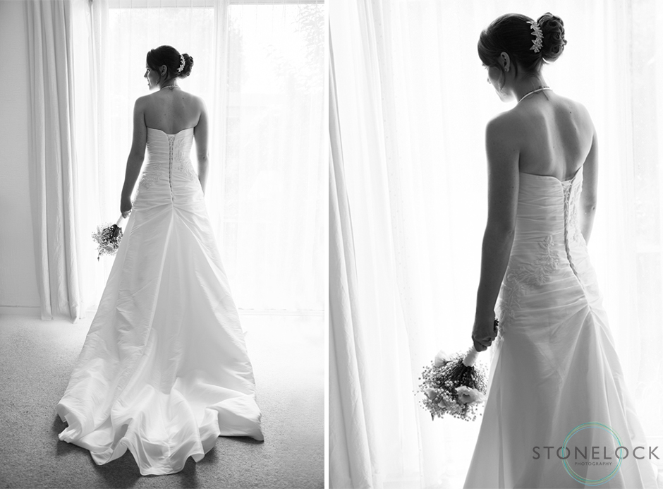 A photography of a bride looks out of the window on her wedding day whilst wearing her wedding dress, the train lays on the floor behind her, in black & white