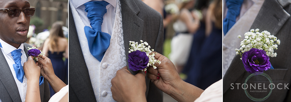 An usher at a wedding puts on his button hole with a little help, the flowers are purple and white