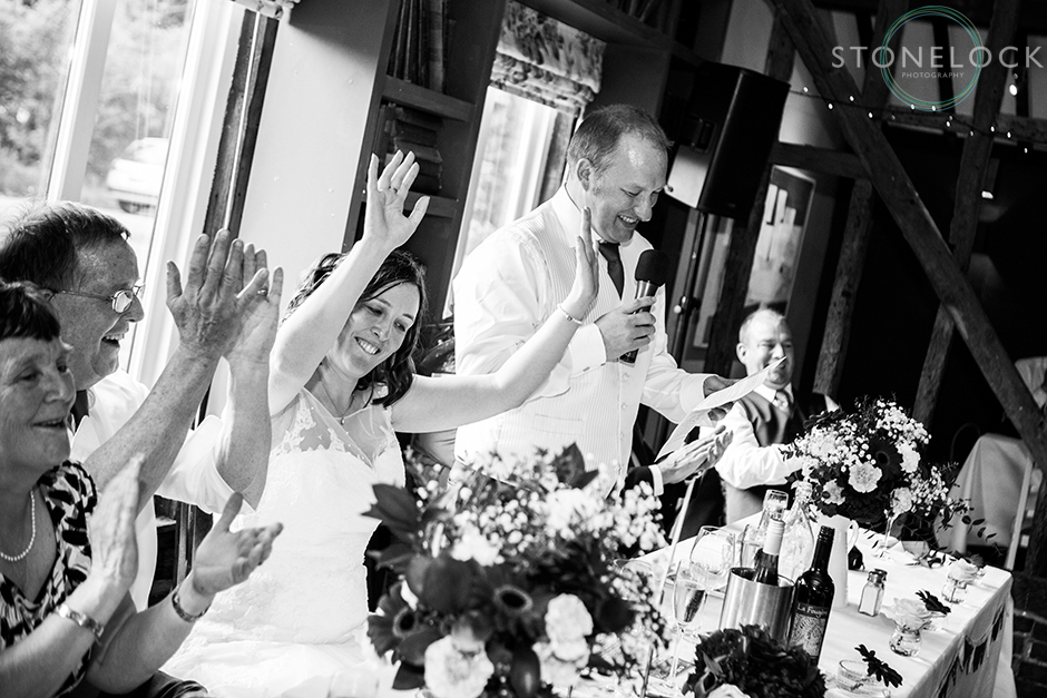 The bride cheers the groom as he gives his wedding speech shot in black and white