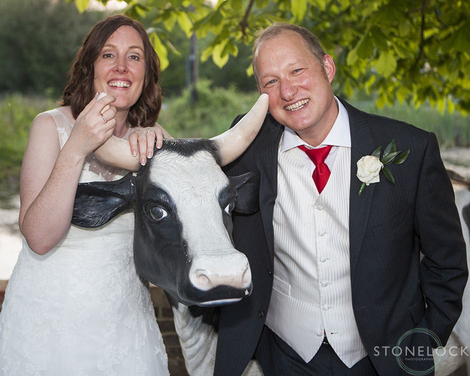 The bride and groom pose next to a life sized model cow