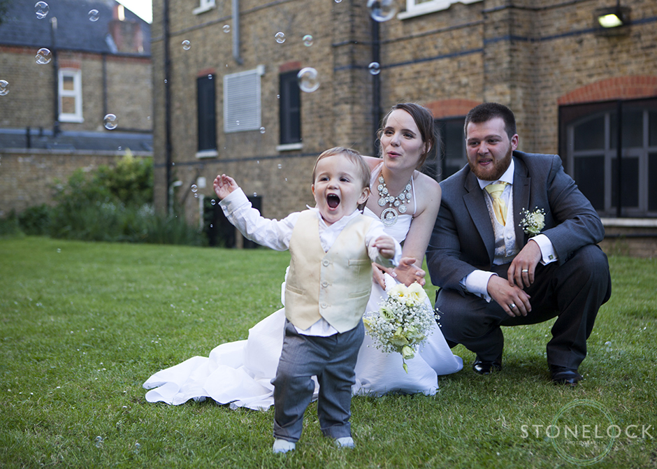 The page boy runs away from the bride and groom chasing bubbles in the sky