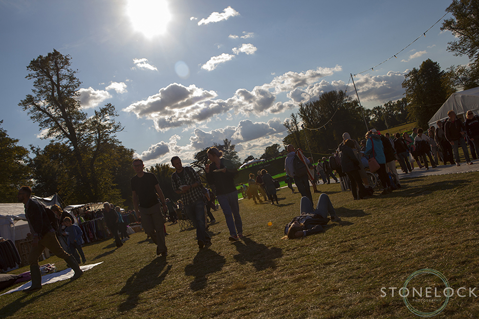 Festival goers walk towards the camera with the sun low in the sky behind them creating long shadows on the ground at Greenbelt Arts Festival at Boughton House