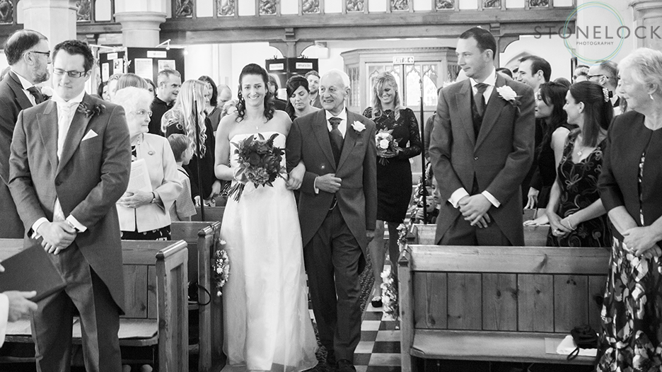 The bride arm in arm with her father walks down the aisle at St Mary's Church in Ewell village 