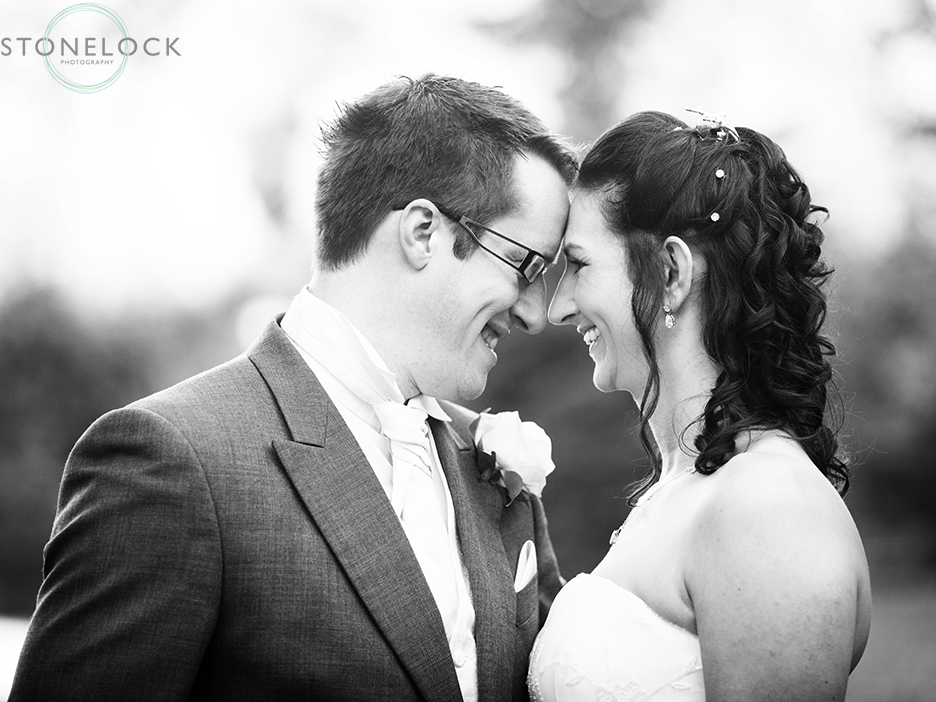 A bride and groom pose for a wedding photo, in black and white they lean towards each other, foreheads touching in a moment of tenderness