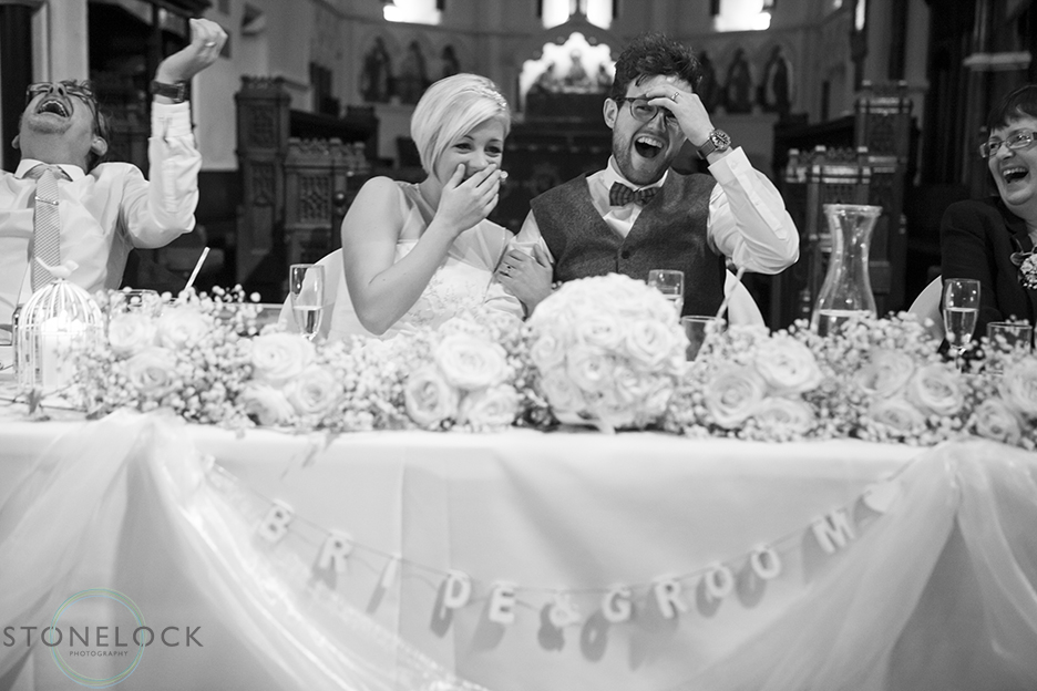 A wedding photo of the bride and groom laughing during the best mans speech at a wedding ceremony at St Mary Magdelene's Church in Bristol