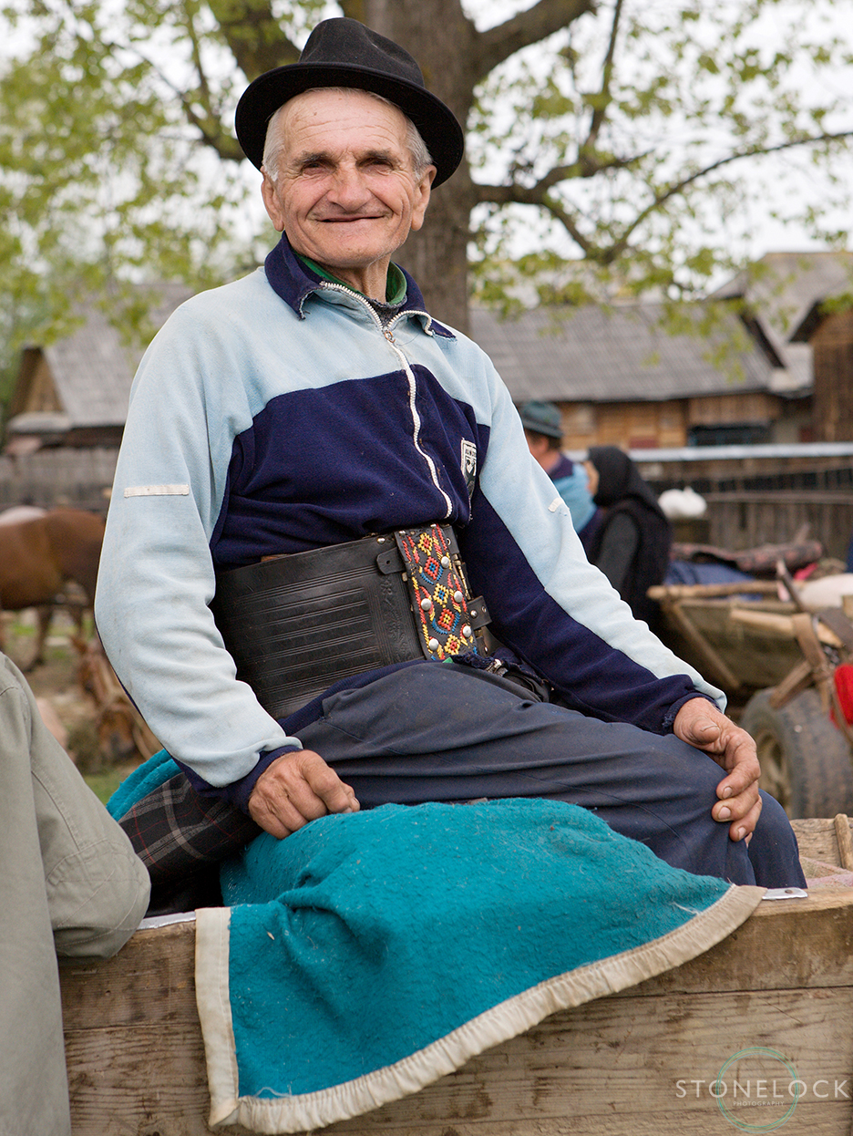 A elderly man sitting on the back of a cart poses for a photo at the Monday morning animal market, Bogdan Voda, Maramures, Romania, 