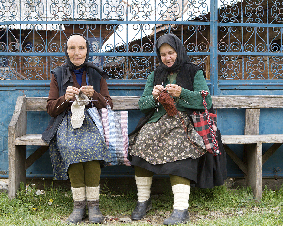 Women sitting on the bench outside their house knitting, Botiza Village, Maramures, Romania, 
