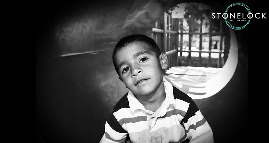 A young boy sits at the front end of a tunnel in a playground and stares into the camera