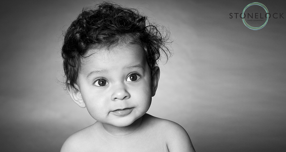 A six month old baby with a neutral expression sits in a photography studio
