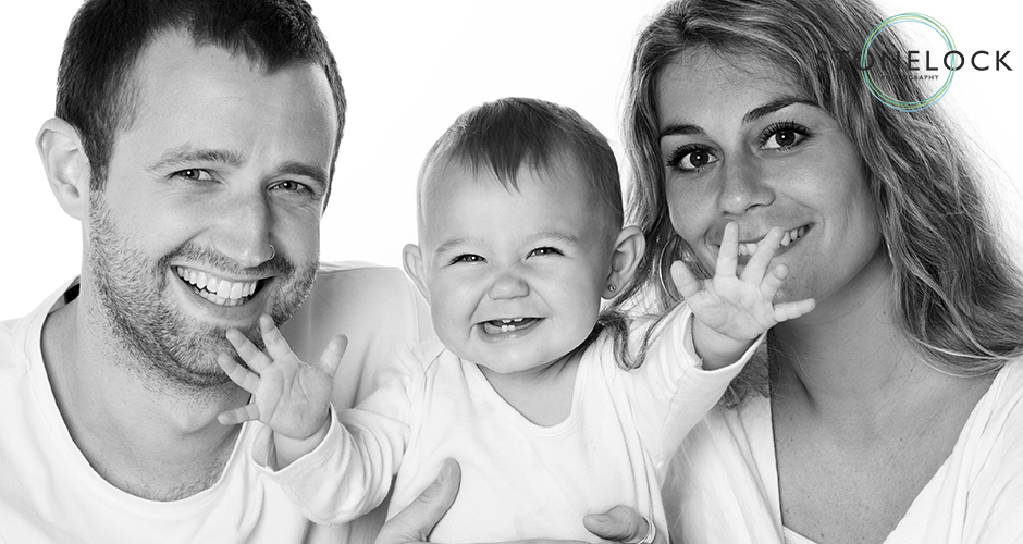 A young family in a photography studio with a baby, the baby reaches out for the camera