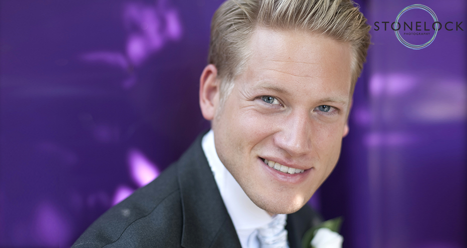 A groom poses in front of a purple background